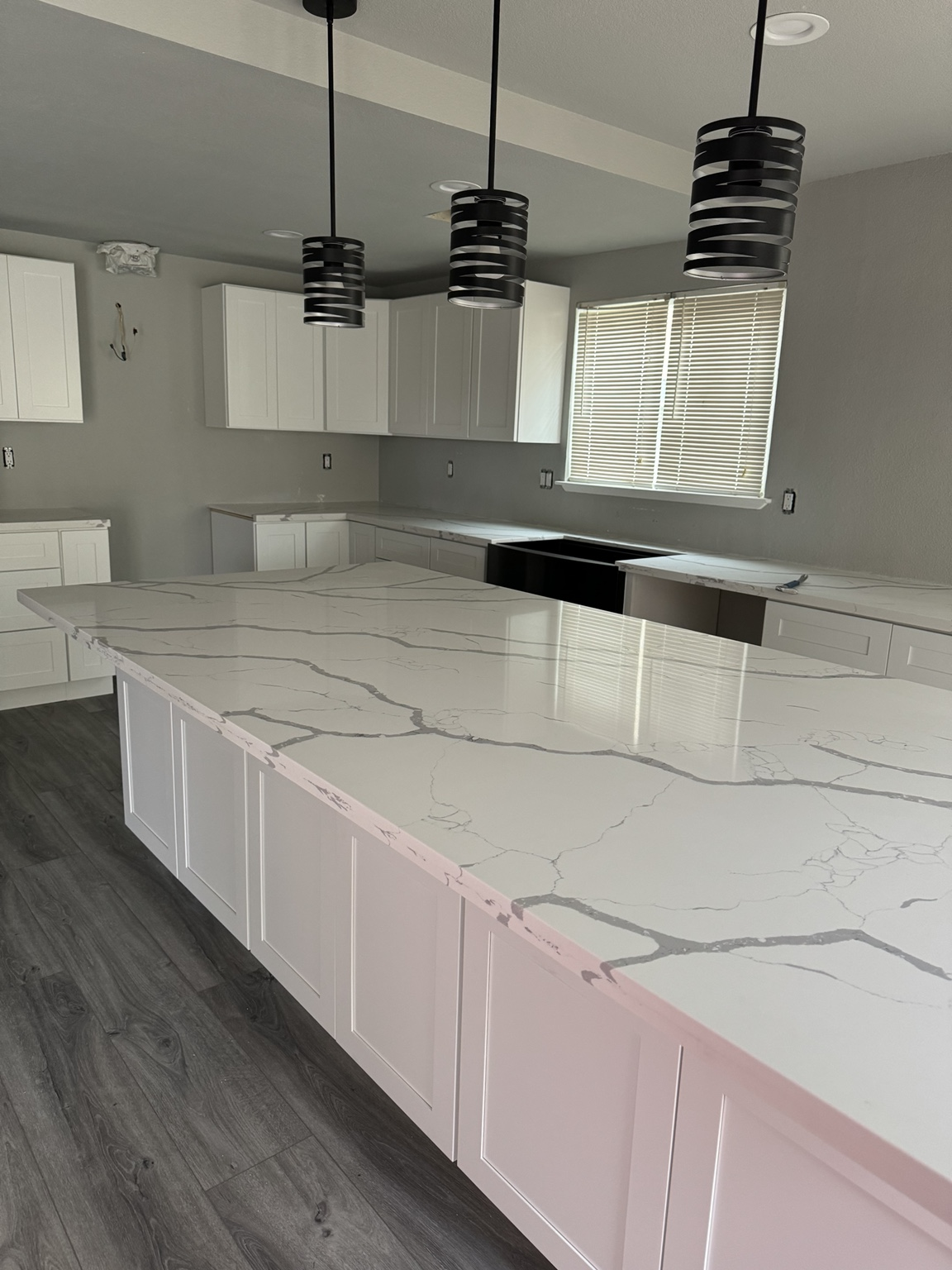 Finished white kitchen remodel with marble-style counters and pendant lights.